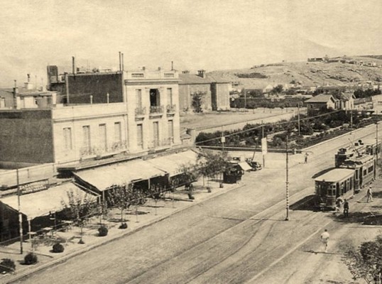 Η στάση Χαροκόπου το 1937. Σταθμευμένο το εξ Αθηνών ερχόμενο τραμ, εν κινήσει το έτερο, αντιθέτου κατευθύνσεως, επί της κεντρικής νησίδος της λεωφόρου Θησέως, μετονομασθείσας σε Ελευθερίου Βενιζέλου, στη διασταύρωση με την οδό Πάριδος, άλλοτε ποτέ δρόμο περιπάτου, η σημερινή οδός Χαροκόπου. Διασώζεται η «Χαροκόπειος Σχολή», αν και αναβαθμισμένη με αποψιλωμένο το αλσύλλιο, καθώς και το γωνιακό δίπατο, το υπόλοιπο τοπίο έχει άρδην μεταμορφωθεί (Αρχείο οικογένειας Κελέφα). Πηγή: Η Αθήνα κάποτε και τώρα.