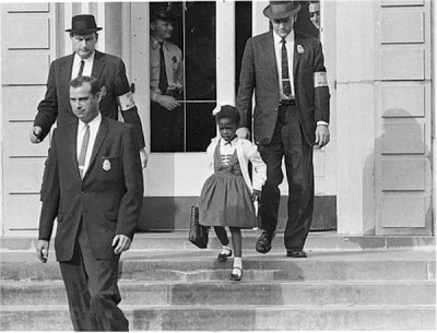 Αστυνομικοί συνοδεύουν την 6χρονη Ρούμπι Μπρίτζις, το πρώτο έγχρωμο παιδί σε σχολείο λευκών. Την “υποδέχθηκαν” με παιδικό φέρετρο και κατάρες. 50 χρόνια μετά την υποδέχθηκαν στον Λευκό Οίκο